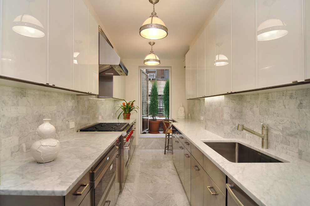 This is an example of a classic galley enclosed kitchen in New York with a submerged sink, flat-panel cabinets, white cabinets, white splashback and stainless steel appliances.