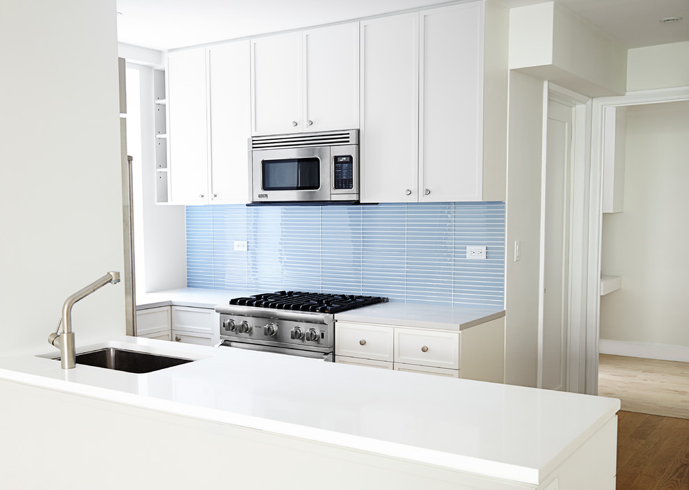 Foto på ett mellanstort funkis kök, med en undermonterad diskho, luckor med infälld panel, vita skåp, bänkskiva i kvarts, blått stänkskydd, stänkskydd i glaskakel, rostfria vitvaror, ljust trägolv och en halv köksö