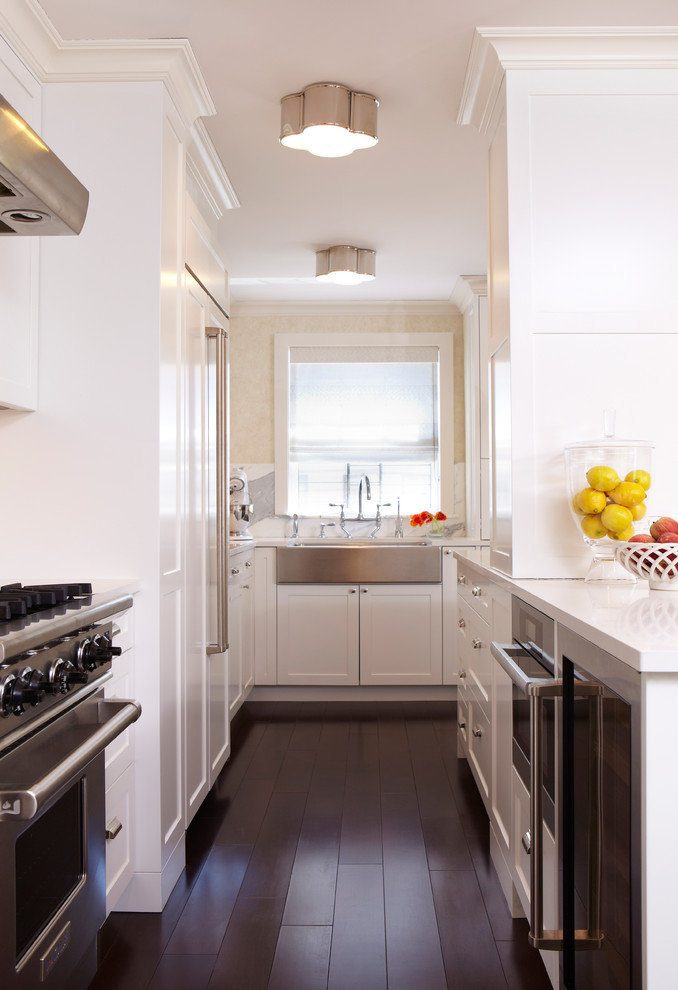 Design ideas for a classic kitchen in New York with a belfast sink, shaker cabinets, white cabinets, stainless steel appliances, dark hardwood flooring and a breakfast bar.