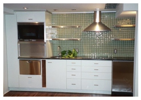 This is an example of a small contemporary single-wall kitchen/diner in New York with a built-in sink, flat-panel cabinets, white cabinets, granite worktops, green splashback, glass tiled splashback, stainless steel appliances and medium hardwood flooring.