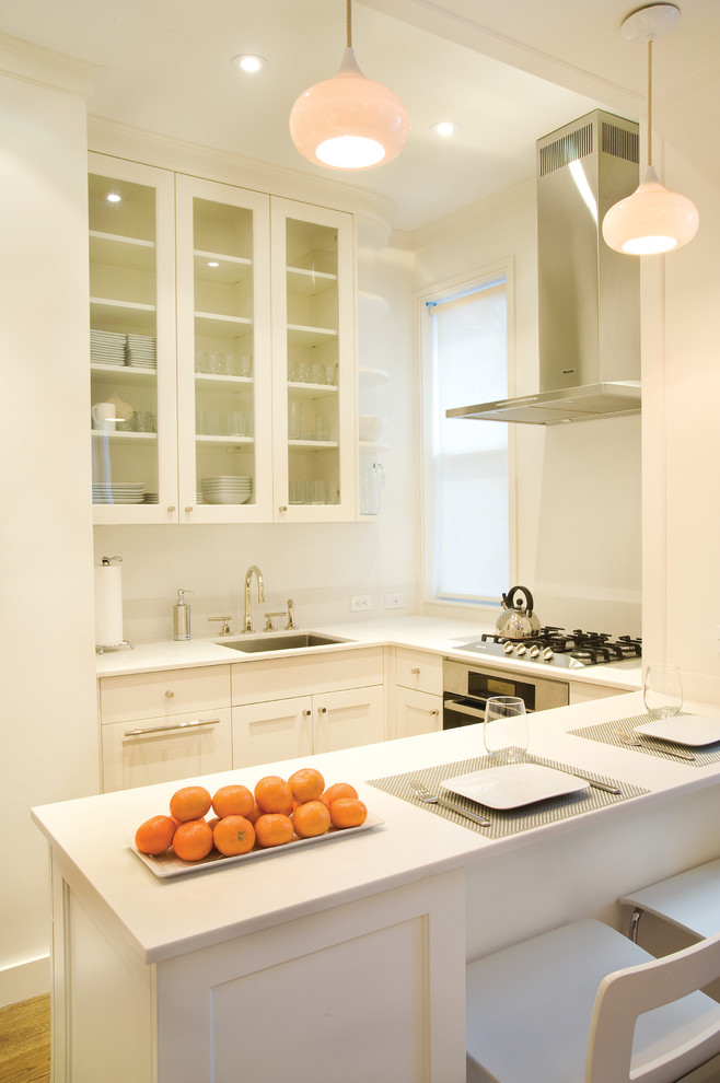 Photo of a small contemporary u-shaped eat-in kitchen in New York with an undermount sink, shaker cabinets, white cabinets, quartz benchtops, stainless steel appliances, light hardwood floors, a peninsula and brown floor.
