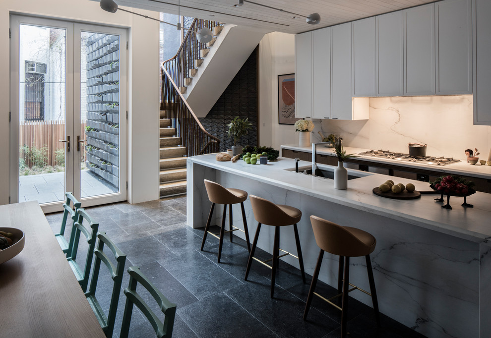 Design ideas for a large contemporary galley kitchen/diner in New York with a submerged sink, recessed-panel cabinets, white splashback, marble splashback, integrated appliances, limestone flooring, an island, black floors, white worktops, white cabinets and marble worktops.