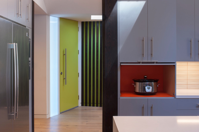 Modern inredning av ett linjärt kök med öppen planlösning, med en undermonterad diskho, släta luckor, grå skåp, grått stänkskydd, stänkskydd i keramik, rostfria vitvaror, ljust trägolv och en köksö