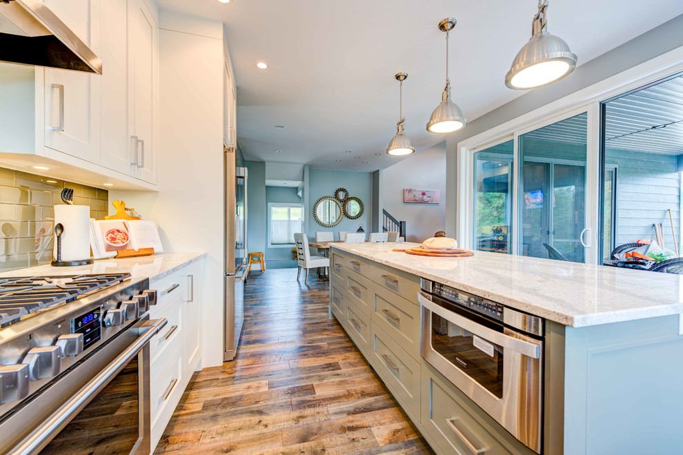 This is an example of a medium sized classic l-shaped kitchen/diner in Vancouver with a submerged sink, flat-panel cabinets, grey cabinets, engineered stone countertops, grey splashback, glass tiled splashback, stainless steel appliances, medium hardwood flooring and an island.