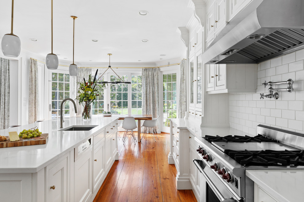 Modern inredning av ett avskilt, mellanstort vit vitt kök, med vita skåp, bänkskiva i kvarts, vitt stänkskydd, stänkskydd i tunnelbanekakel, mellanmörkt trägolv och en köksö
