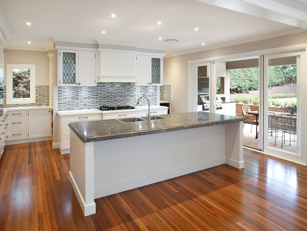Design ideas for a large traditional galley kitchen pantry in Sydney with a double-bowl sink, shaker cabinets, white cabinets, engineered stone countertops, multi-coloured splashback, porcelain splashback, integrated appliances, medium hardwood flooring and an island.