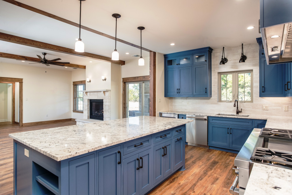 This is an example of a medium sized farmhouse u-shaped open plan kitchen in Austin with a submerged sink, shaker cabinets, blue cabinets, granite worktops, white splashback, porcelain splashback, stainless steel appliances, vinyl flooring, an island, brown floors and blue worktops.
