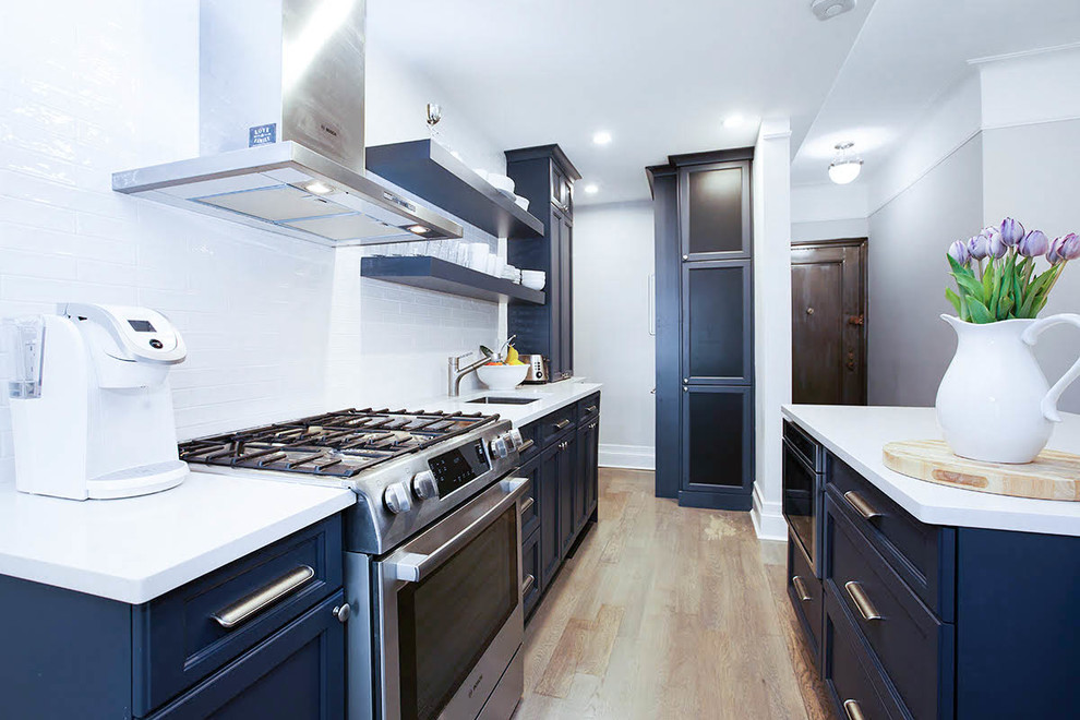 Photo of a large traditional galley kitchen/diner in New York with a submerged sink, recessed-panel cabinets, blue cabinets, wood worktops, white splashback, metro tiled splashback, stainless steel appliances, plywood flooring and an island.