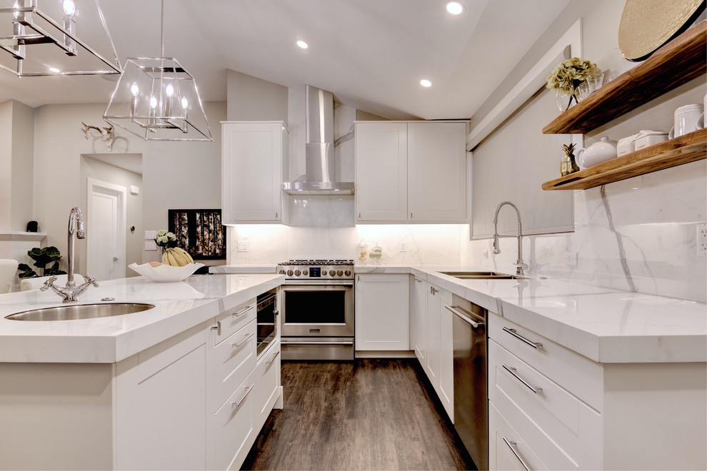 Photo of a medium sized traditional kitchen/diner in Calgary with a double-bowl sink, flat-panel cabinets, white cabinets, marble worktops, white splashback, stainless steel appliances, dark hardwood flooring and an island.