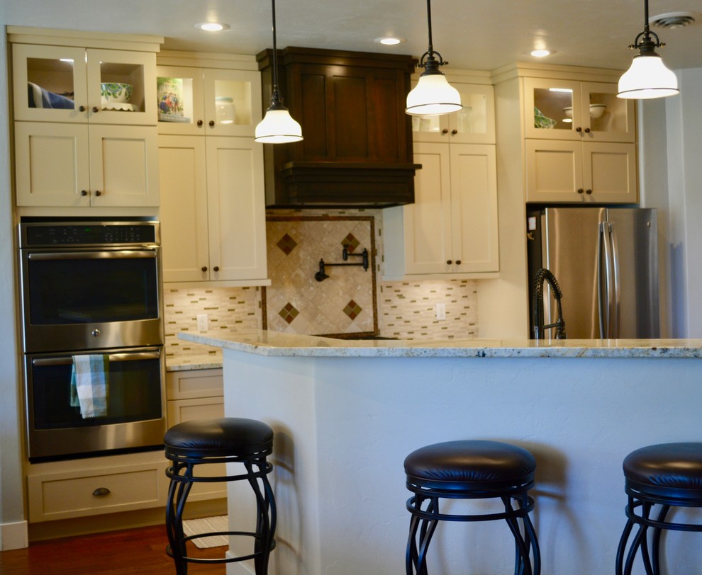 Inredning av ett klassiskt mellanstort kök, med en undermonterad diskho, skåp i shakerstil, vita skåp, granitbänkskiva, beige stänkskydd, stänkskydd i mosaik, rostfria vitvaror, mellanmörkt trägolv, en halv köksö och brunt golv
