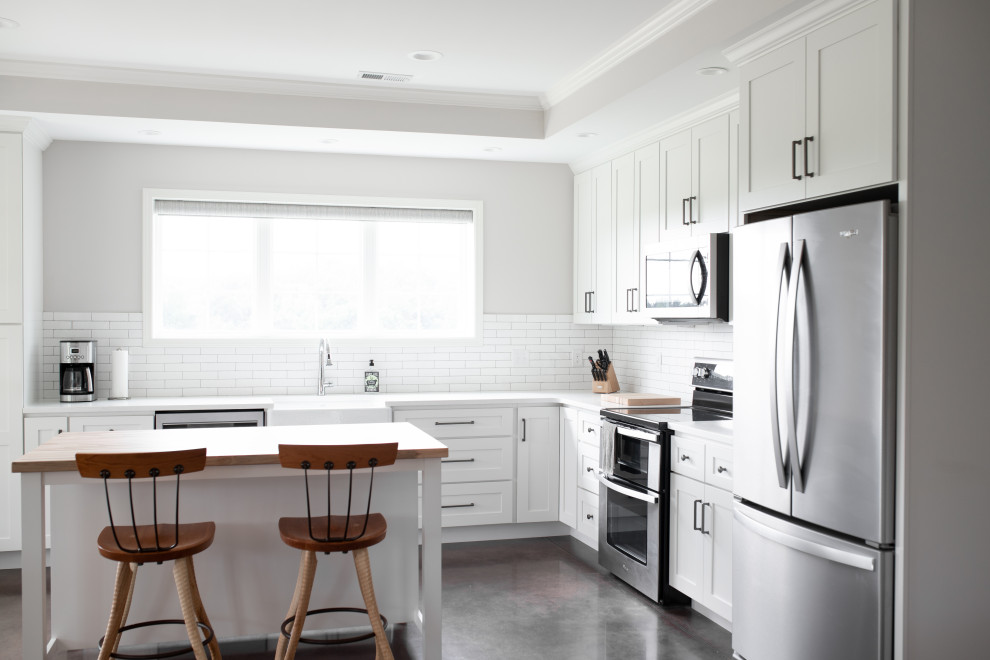 Idéer för mellanstora lantliga vitt kök, med en rustik diskho, skåp i shakerstil, vita skåp, bänkskiva i kvarts, vitt stänkskydd, stänkskydd i keramik, rostfria vitvaror, betonggolv, en köksö och brunt golv