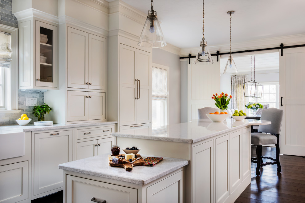 Inspiration for a mid-sized timeless l-shaped dark wood floor and brown floor open concept kitchen remodel in Boston with a farmhouse sink, beaded inset cabinets, white cabinets, marble countertops, gray backsplash, stone tile backsplash, stainless steel appliances and an island