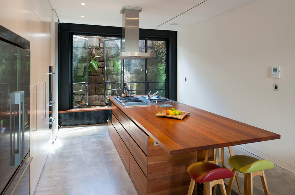Aménagement d'une cuisine parallèle contemporaine avec un placard à porte plane, des portes de placard blanches, un plan de travail en bois, sol en béton ciré et îlot.