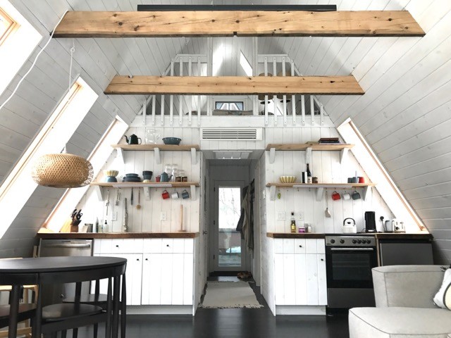 Photo of a small rural single-wall open plan kitchen in New York with a built-in sink, stainless steel appliances, louvered cabinets, white cabinets, wood worktops, white splashback, wood splashback and no island.