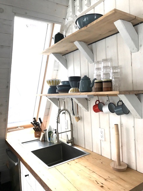 Foto på ett litet lantligt linjärt kök med öppen planlösning, med rostfria vitvaror, en nedsänkt diskho, luckor med lamellpanel, vita skåp, träbänkskiva, vitt stänkskydd och stänkskydd i trä