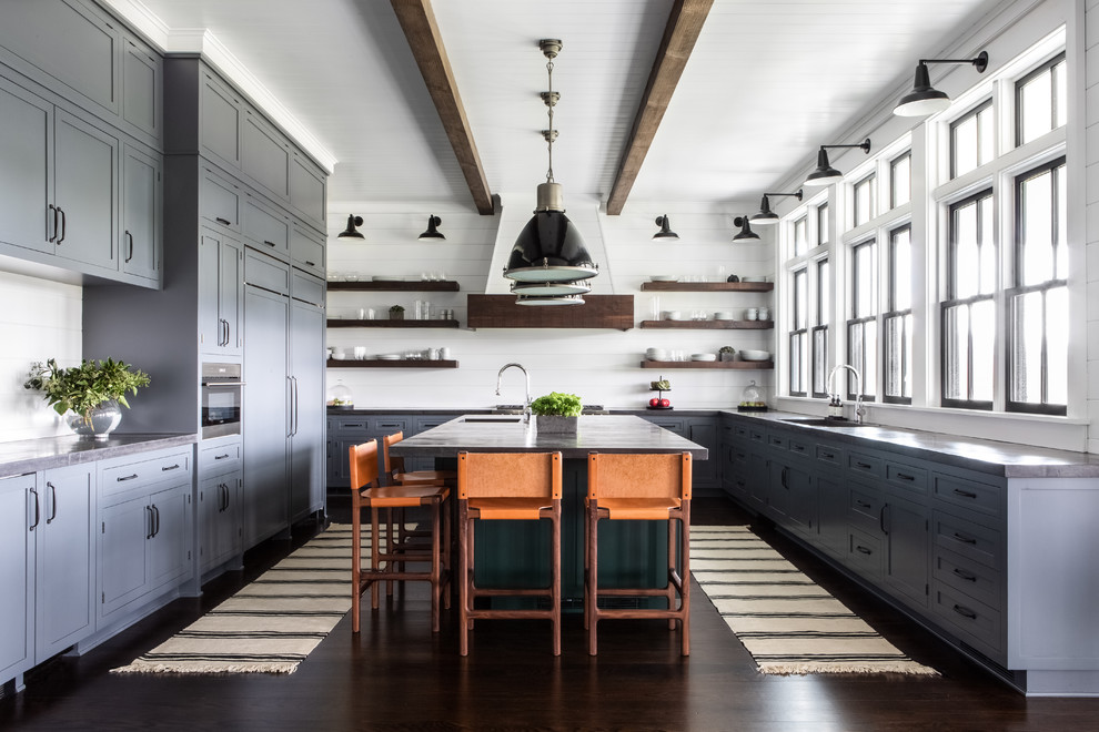 Lantlig inredning av ett stort grå grått kök, med en undermonterad diskho, luckor med infälld panel, grå skåp, bänkskiva i betong, vitt stänkskydd, stänkskydd i trä, integrerade vitvaror, mörkt trägolv, en köksö och brunt golv