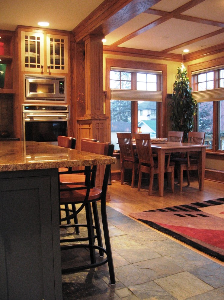 Eat-in kitchen - mid-sized craftsman l-shaped slate floor eat-in kitchen idea in Minneapolis with an undermount sink, recessed-panel cabinets, medium tone wood cabinets, granite countertops, gray backsplash, stainless steel appliances and an island