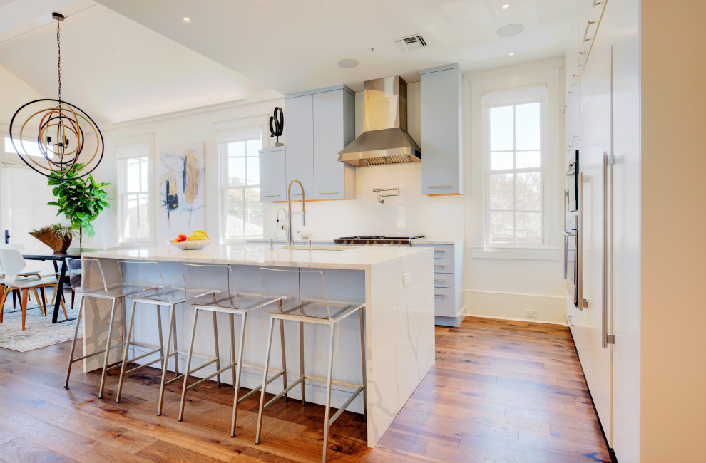 Mittelgroße Moderne Küche in L-Form mit flächenbündigen Schrankfronten, blauen Schränken, Küchenrückwand in Weiß, Elektrogeräten mit Frontblende, braunem Holzboden, Kücheninsel und weißer Arbeitsplatte in New Orleans