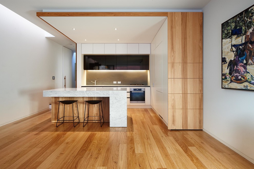 Inspiration pour une cuisine design avec un placard à porte plane, un sol en bois brun, îlot et des portes de placard blanches.