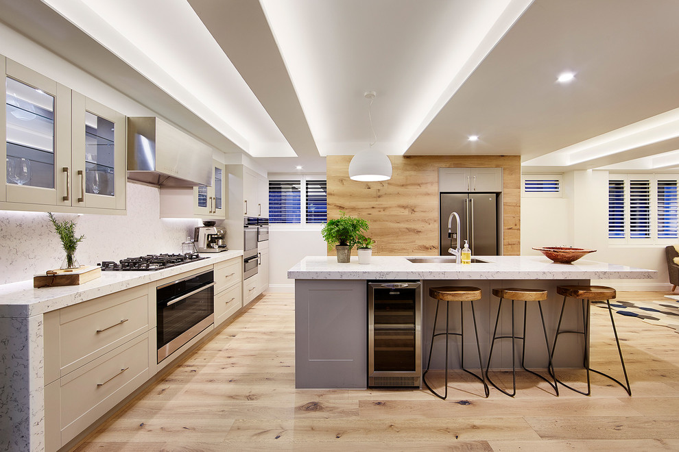 Exempel på ett stort modernt kök och matrum, med en undermonterad diskho, luckor med infälld panel, grå skåp, bänkskiva i kvarts, stänkskydd i sten, rostfria vitvaror, ljust trägolv och en köksö