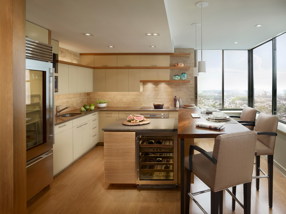 This is an example of a contemporary l-shaped kitchen in Philadelphia with a submerged sink, flat-panel cabinets, beige cabinets, beige splashback, stainless steel appliances, medium hardwood flooring, an island, quartz worktops and limestone splashback.