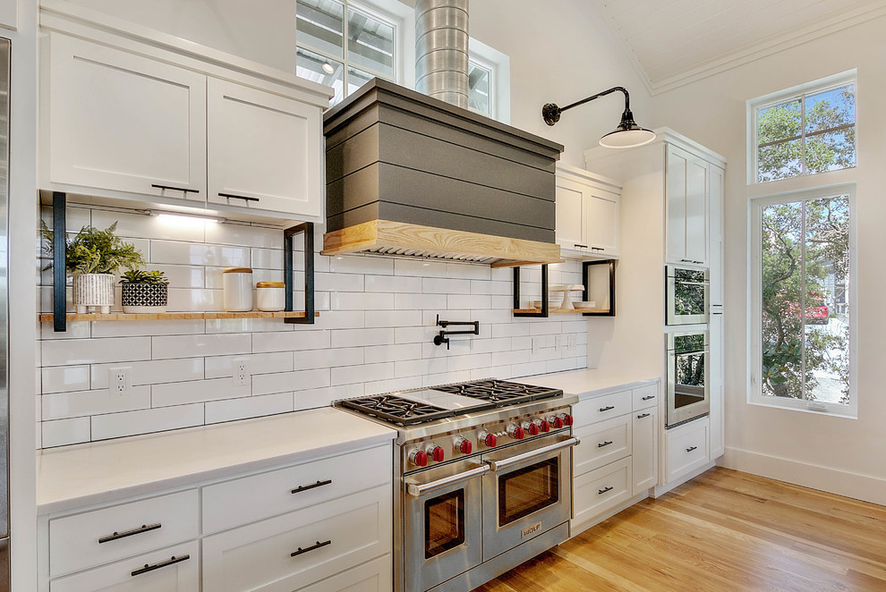 Example of a beach style galley medium tone wood floor and brown floor kitchen design in Miami with shaker cabinets, white cabinets, white backsplash, subway tile backsplash, stainless steel appliances, no island and white countertops