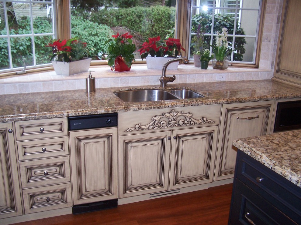 Example of a large classic u-shaped dark wood floor eat-in kitchen design in Vancouver with an undermount sink, raised-panel cabinets, distressed cabinets, granite countertops, beige backsplash, ceramic backsplash, paneled appliances and an island