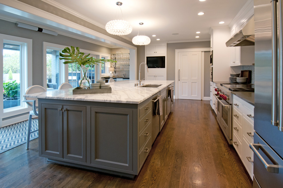 Photo of a large traditional galley open plan kitchen in Seattle with a double-bowl sink, recessed-panel cabinets, white cabinets, marble worktops, multi-coloured splashback, stone slab splashback, stainless steel appliances, light hardwood flooring and an island.
