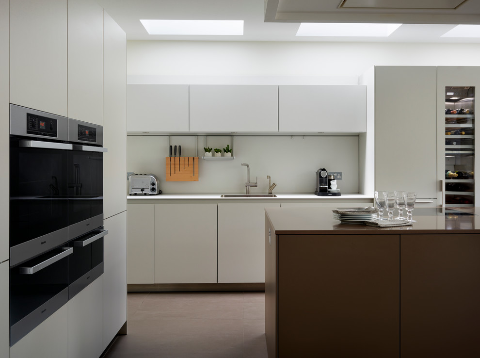 Exempel på ett modernt kök, med en enkel diskho, släta luckor, vita skåp, vitt stänkskydd, rostfria vitvaror och en köksö