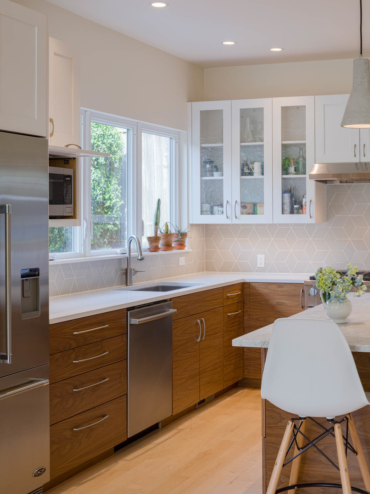 Example of a mid-sized transitional l-shaped light wood floor eat-in kitchen design in Seattle with an undermount sink, glass-front cabinets, quartz countertops, gray backsplash, ceramic backsplash, stainless steel appliances, an island and white countertops