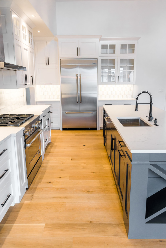 Inredning av ett lantligt mellanstort l-kök, med en undermonterad diskho, luckor med infälld panel, vita skåp, bänkskiva i kvarts, vitt stänkskydd, stänkskydd i keramik, rostfria vitvaror, ljust trägolv, en köksö och flerfärgat golv