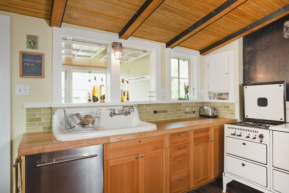 Idée de décoration pour une cuisine américaine design en L et bois brun avec un évier de ferme, un placard à porte shaker, un plan de travail en bois, une crédence verte, une crédence en céramique, un électroménager en acier inoxydable et un sol en bois brun.