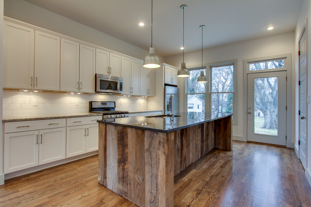 Bild på ett mellanstort funkis kök, med en undermonterad diskho, skåp i shakerstil, vita skåp, vitt stänkskydd, stänkskydd i keramik, rostfria vitvaror, mellanmörkt trägolv, en köksö och brunt golv