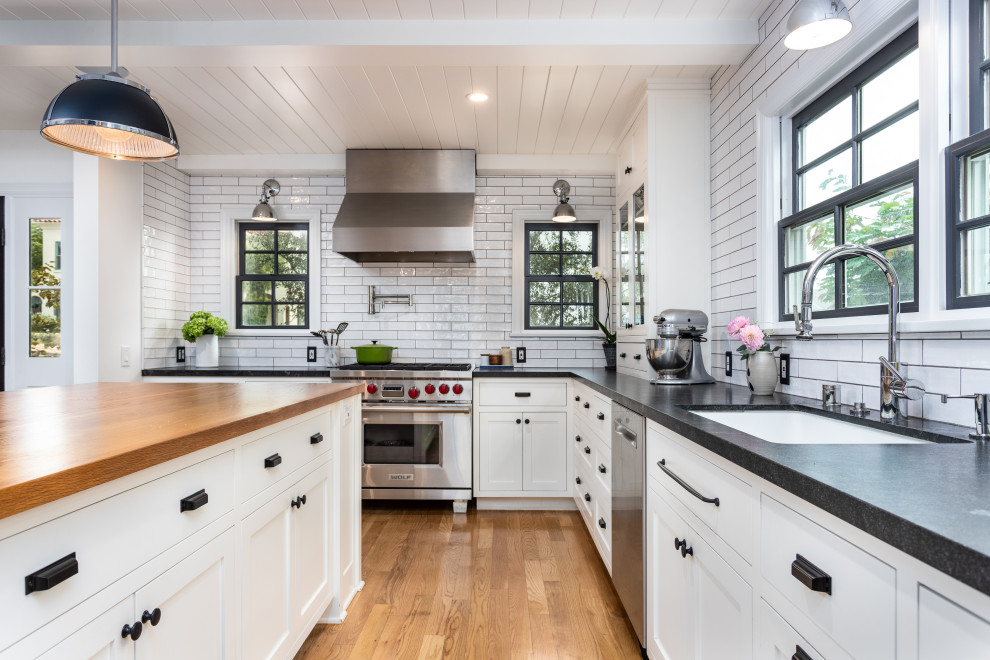 Example of a mid-sized cottage u-shaped light wood floor, brown floor and shiplap ceiling eat-in kitchen design in Los Angeles with an undermount sink, shaker cabinets, white cabinets, quartzite countertops, white backsplash, subway tile backsplash, stainless steel appliances, an island and black countertops