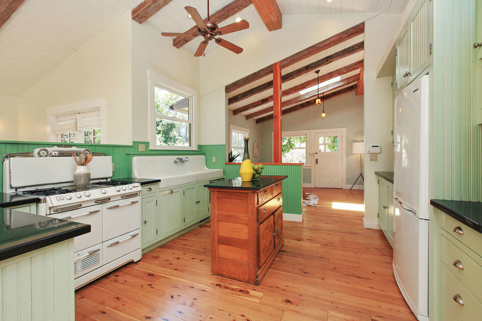 На фото: параллельная кухня-гостиная в стиле кантри с с полувстраиваемой мойкой (с передним бортиком), зелеными фасадами, белой техникой, паркетным полом среднего тона и островом