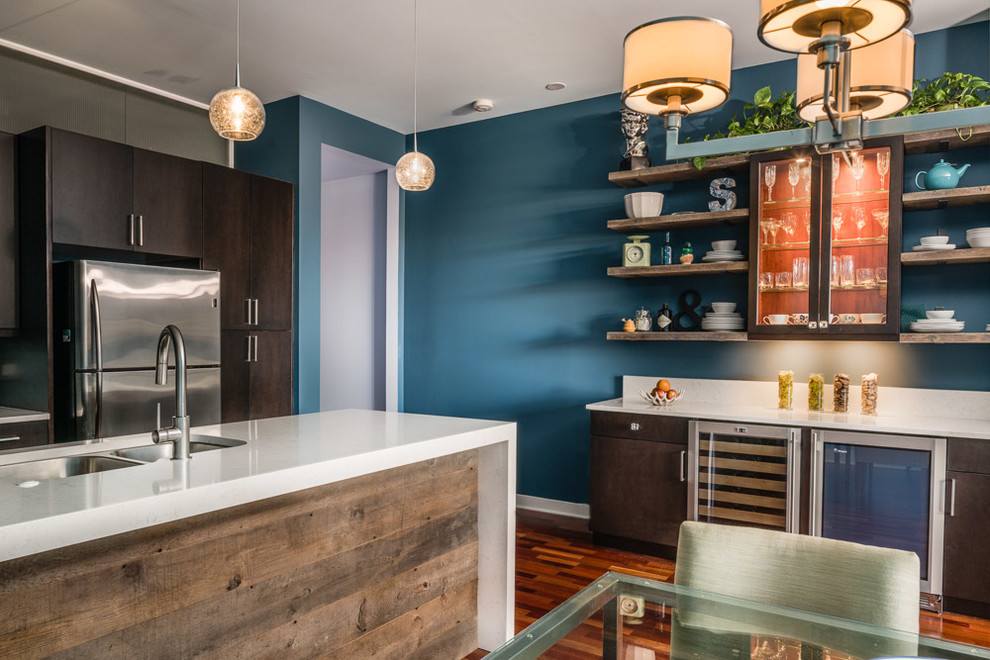 Modern inredning av ett litet kök, med en dubbel diskho, släta luckor, bruna skåp, bänkskiva i kvarts, blått stänkskydd, stänkskydd i glaskakel, rostfria vitvaror, mellanmörkt trägolv och en halv köksö