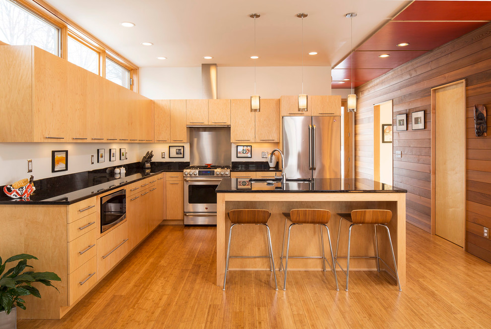 На фото: угловая кухня в стиле модернизм с плоскими фасадами, техникой из нержавеющей стали и барной стойкой с