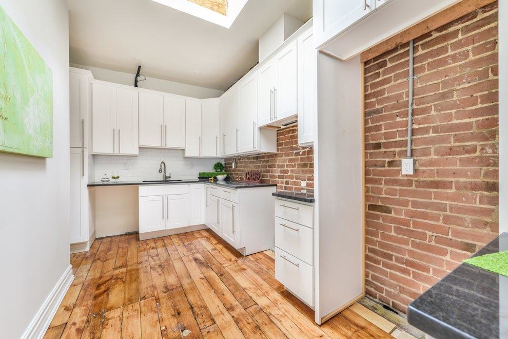 Inspiration pour une cuisine américaine urbaine avec un placard à porte shaker, des portes de placard blanches, un électroménager en acier inoxydable et un sol en bois brun.