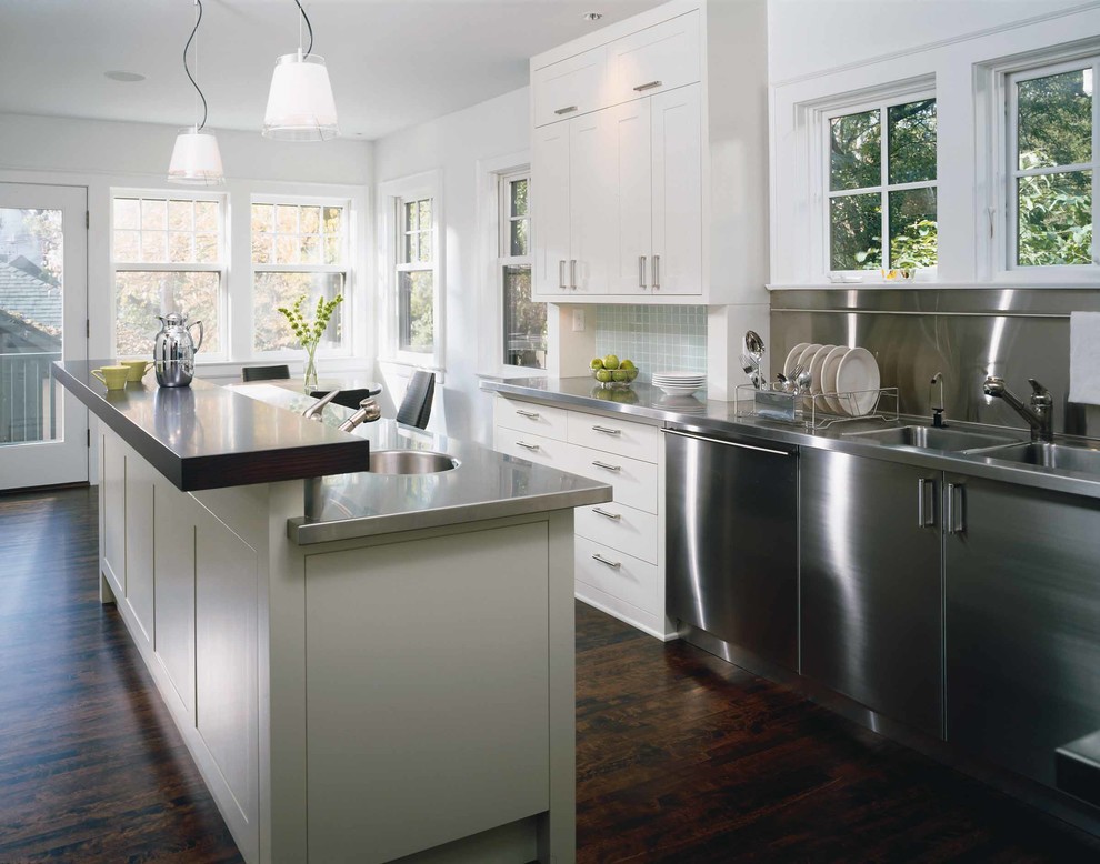 Design ideas for a traditional kitchen/diner in Minneapolis with a submerged sink, flat-panel cabinets, white cabinets, stainless steel worktops, metallic splashback, metal splashback, stainless steel appliances, dark hardwood flooring and an island.
