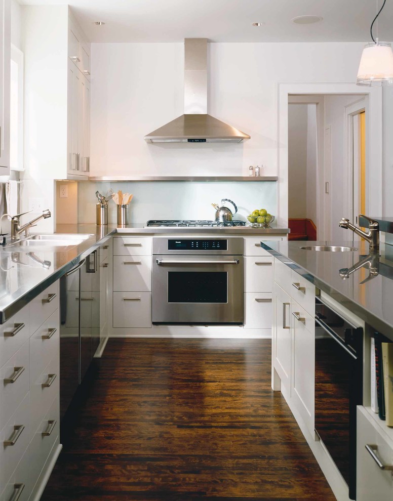 Idéer för att renovera ett funkis kök, med en undermonterad diskho, släta luckor, vita skåp, bänkskiva i rostfritt stål, stänkskydd med metallisk yta, rostfria vitvaror, mörkt trägolv, stänkskydd i metallkakel och en köksö