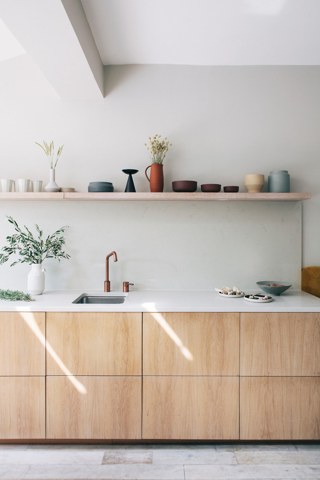 Cette photo montre une cuisine linéaire tendance en bois clair avec un évier encastré, un placard à porte plane, une crédence grise et un plan de travail blanc.