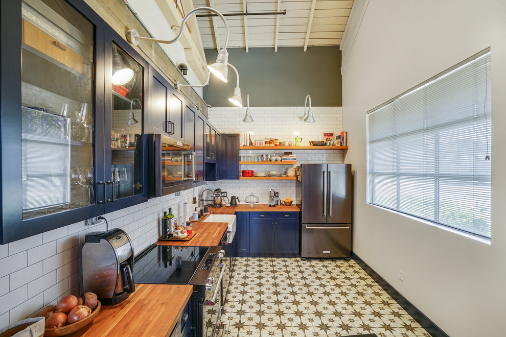 Inspiration for a mid-sized transitional l-shaped multicolored floor and ceramic tile enclosed kitchen remodel in San Francisco with a farmhouse sink, shaker cabinets, blue cabinets, wood countertops, white backsplash, subway tile backsplash, stainless steel appliances, brown countertops and no island