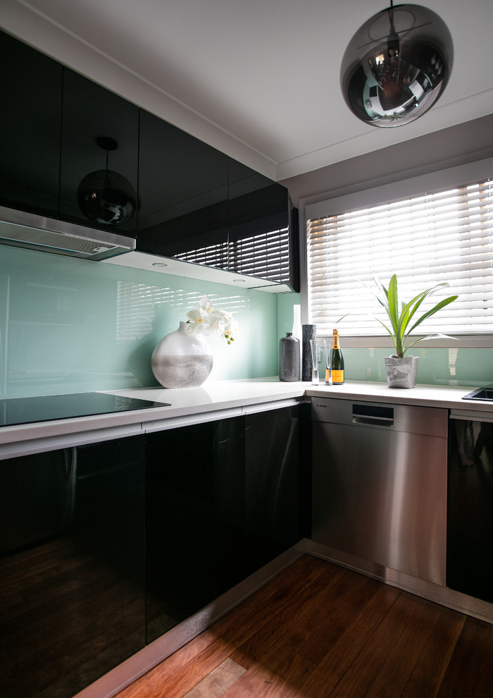 Idée de décoration pour une cuisine minimaliste avec un évier posé, un placard à porte plane, des portes de placard noires, une crédence bleue, une crédence en feuille de verre, un électroménager en acier inoxydable et un sol en bois brun.