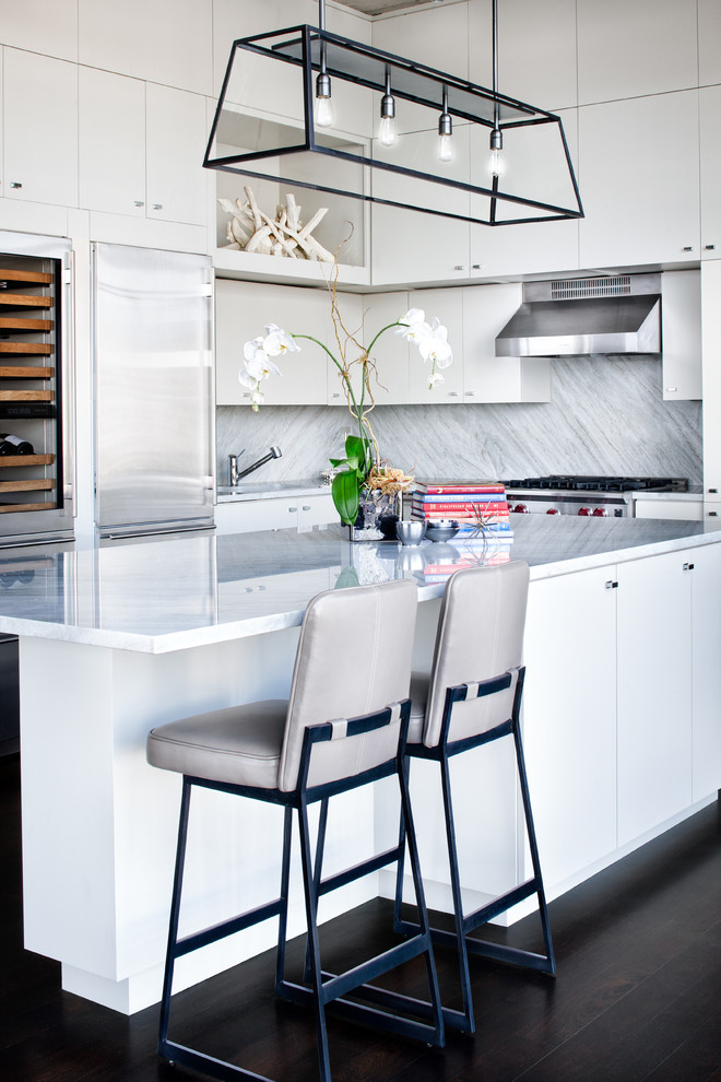 Moderne Küche mit flächenbündigen Schrankfronten, weißen Schränken, Küchenrückwand in Grau, Küchengeräten aus Edelstahl, dunklem Holzboden und Kücheninsel in Austin