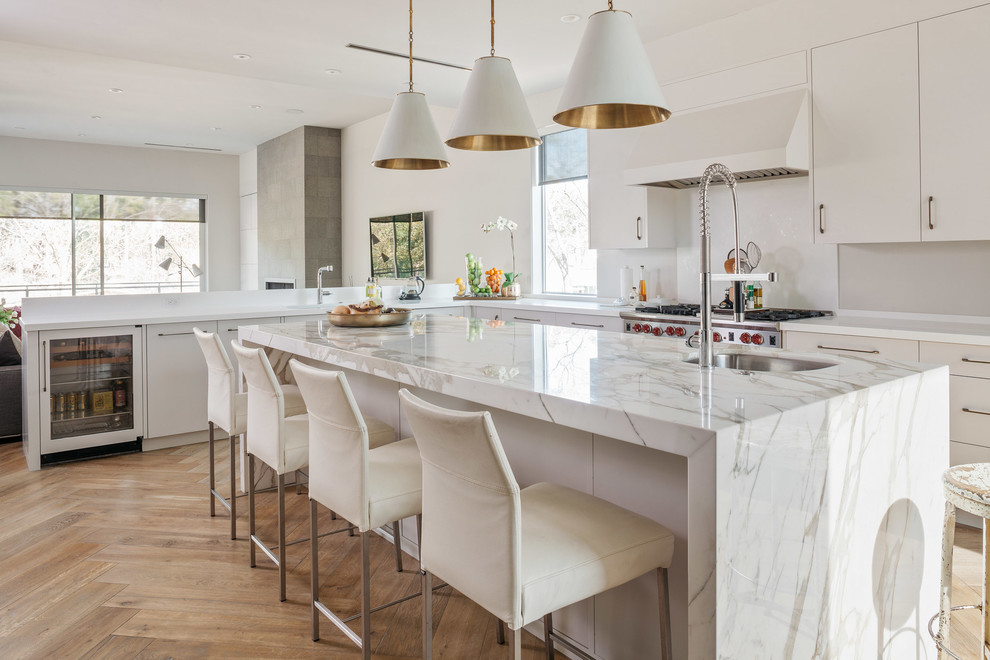 Idée de décoration pour une cuisine design en L avec un évier encastré, un placard à porte plane, des portes de placard blanches, une crédence blanche, un électroménager en acier inoxydable, un sol en bois brun, îlot et un sol beige.