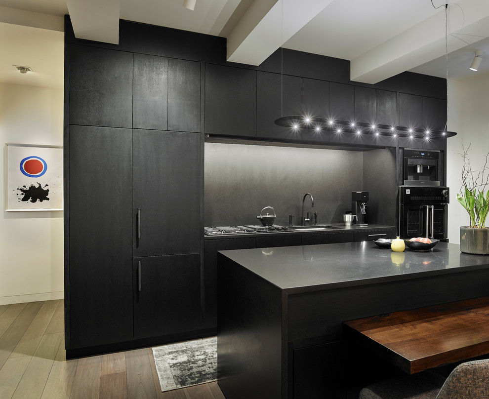 Идея дизайна: прямая кухня-гостиная среднего размера в стиле модернизм с врезной мойкой, плоскими фасадами, черными фасадами, серым фартуком, светлым паркетным полом, островом, столешницей из акрилового камня и черной техникой