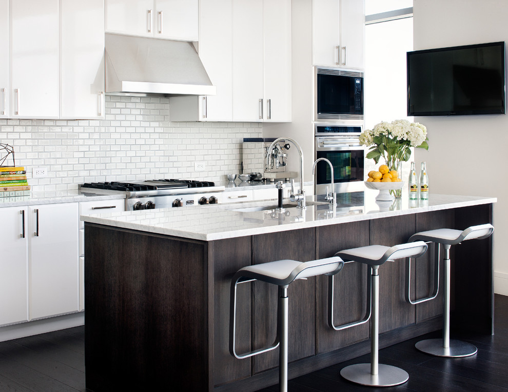 Zweizeilige Moderne Küche mit Unterbauwaschbecken, flächenbündigen Schrankfronten, weißen Schränken, Küchenrückwand in Weiß, Rückwand aus Metrofliesen, Küchengeräten aus Edelstahl, dunklem Holzboden und Kücheninsel in Austin
