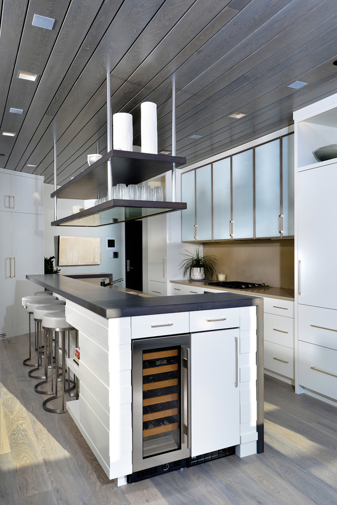 На фото: параллельная кухня в современном стиле с плоскими фасадами, белыми фасадами, техникой под мебельный фасад, темным паркетным полом и островом