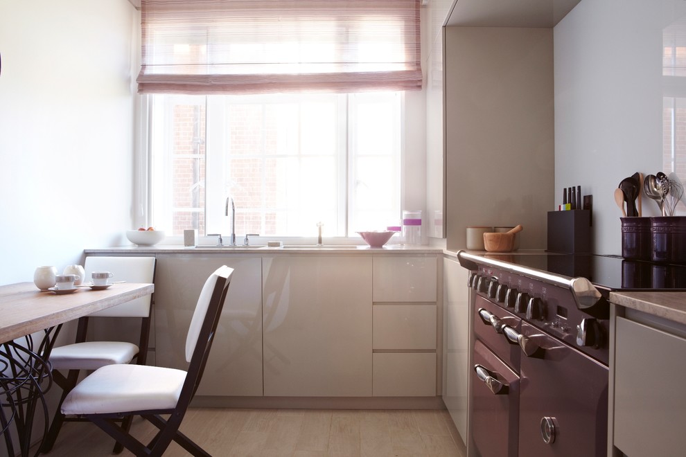 This is an example of a small contemporary l-shaped enclosed kitchen in London with a single-bowl sink, flat-panel cabinets, beige cabinets, limestone worktops, glass sheet splashback, coloured appliances, porcelain flooring and no island.