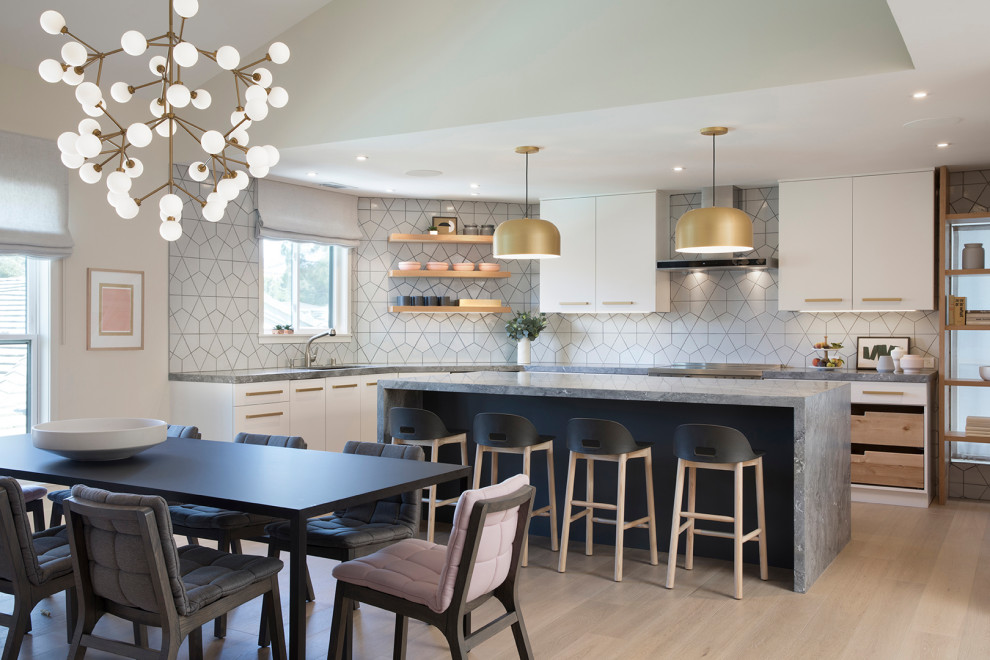 Contemporary l-shaped kitchen/diner in San Francisco with a submerged sink, flat-panel cabinets, white cabinets, white splashback, light hardwood flooring, an island, beige floors and grey worktops.